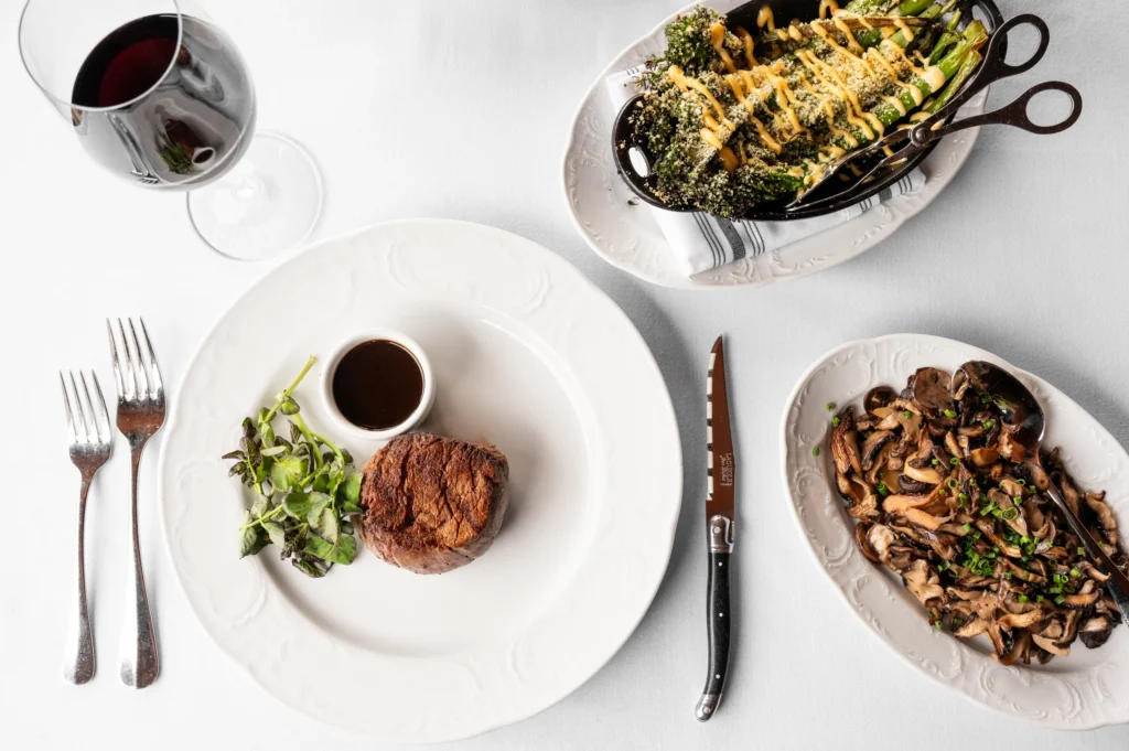 /Alt Top down view of filet mignon on a plate, roasted asparagus, sautéed mushrooms, and a glass of red wine.