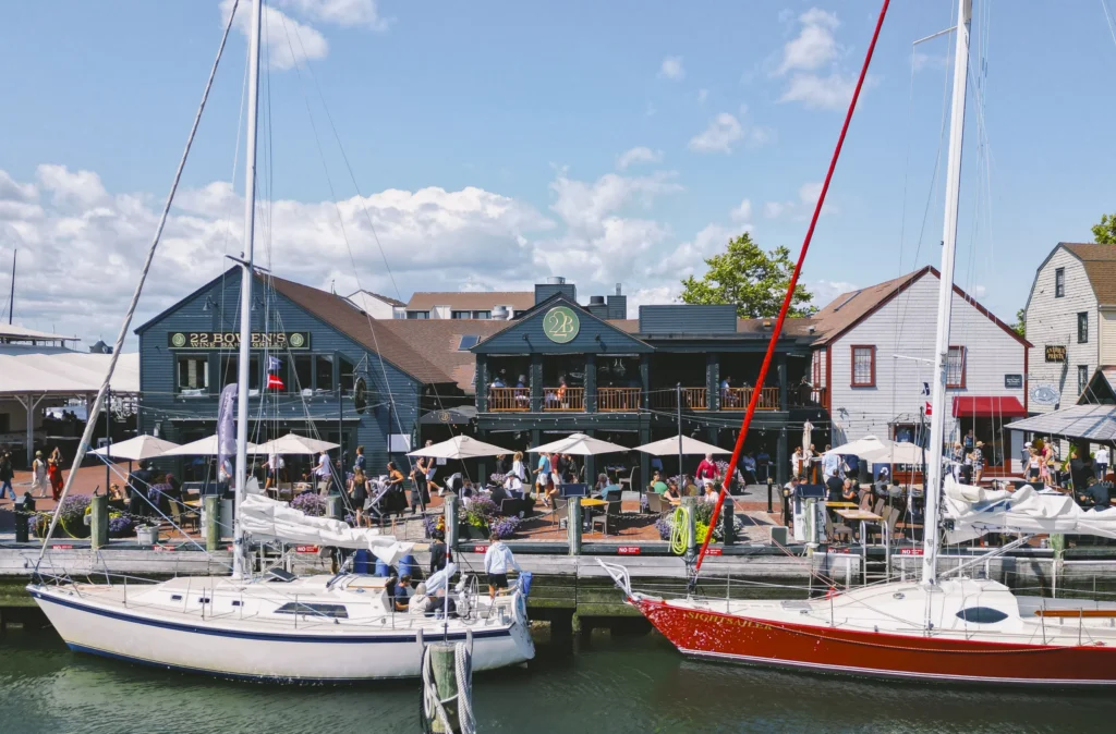 Sailboats docked at the harbor in front of outdoor patio dining area on a sunny day.