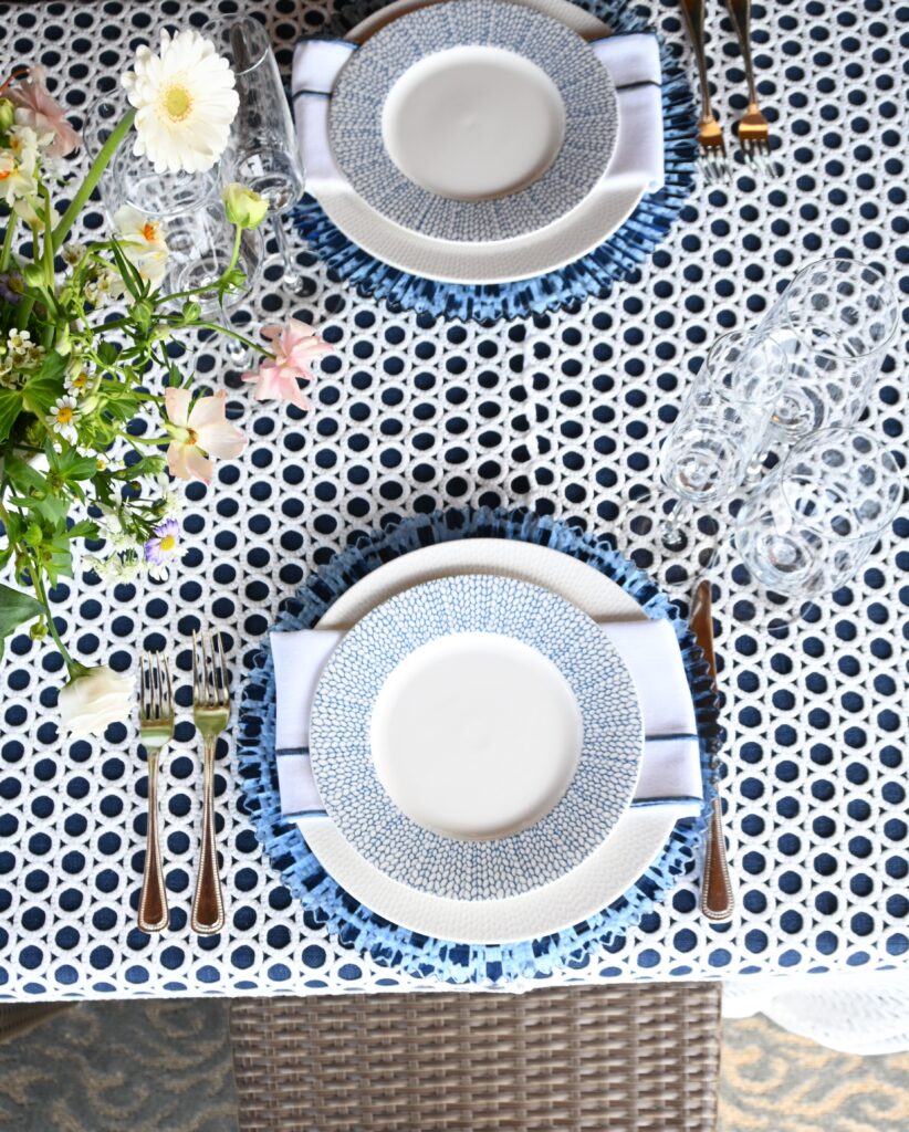 Top down view of a table set with patterned blue plates, napkins, silverware, glassware, and fresh flowers.
