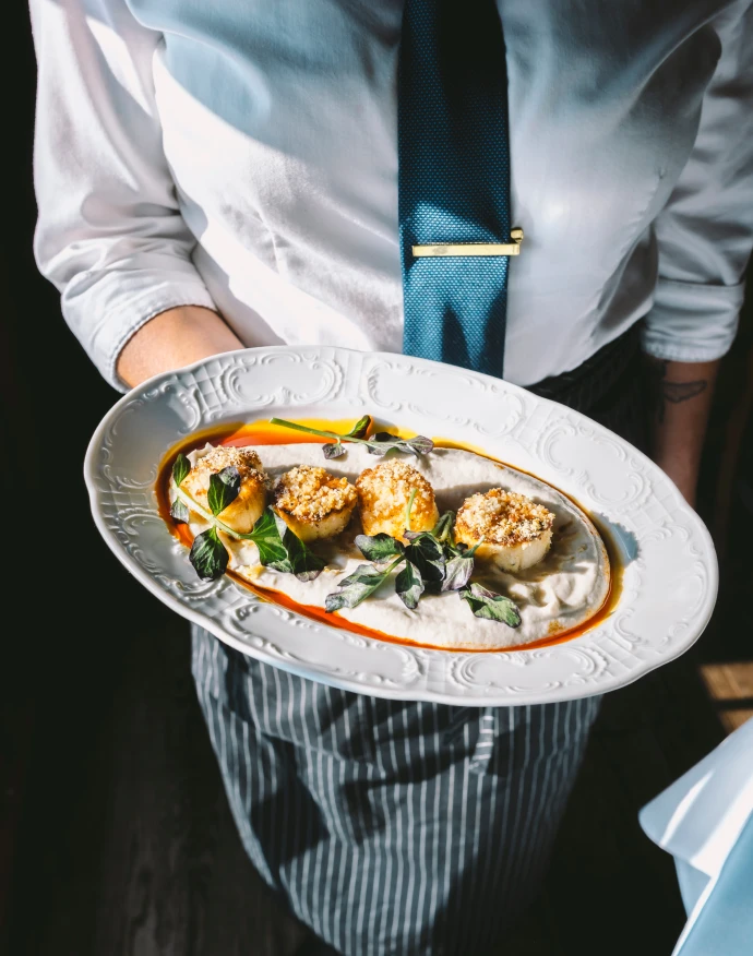 As server holds a plate of seared scallops