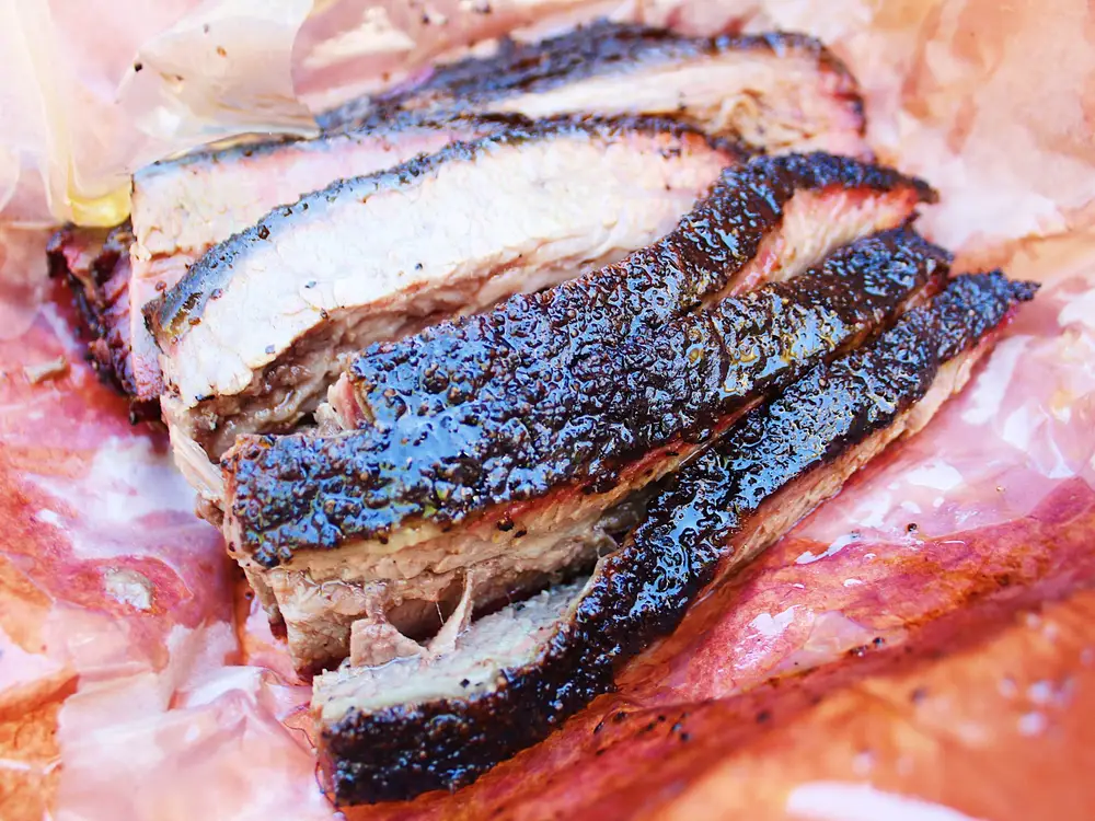 A close-up view of sliced smoked brisket served on pink butcher paper.