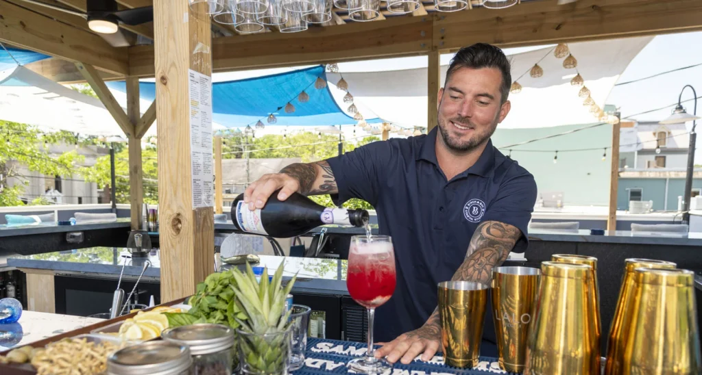 A bartender pours, a sparkling wine cocktail on an outdoor patio