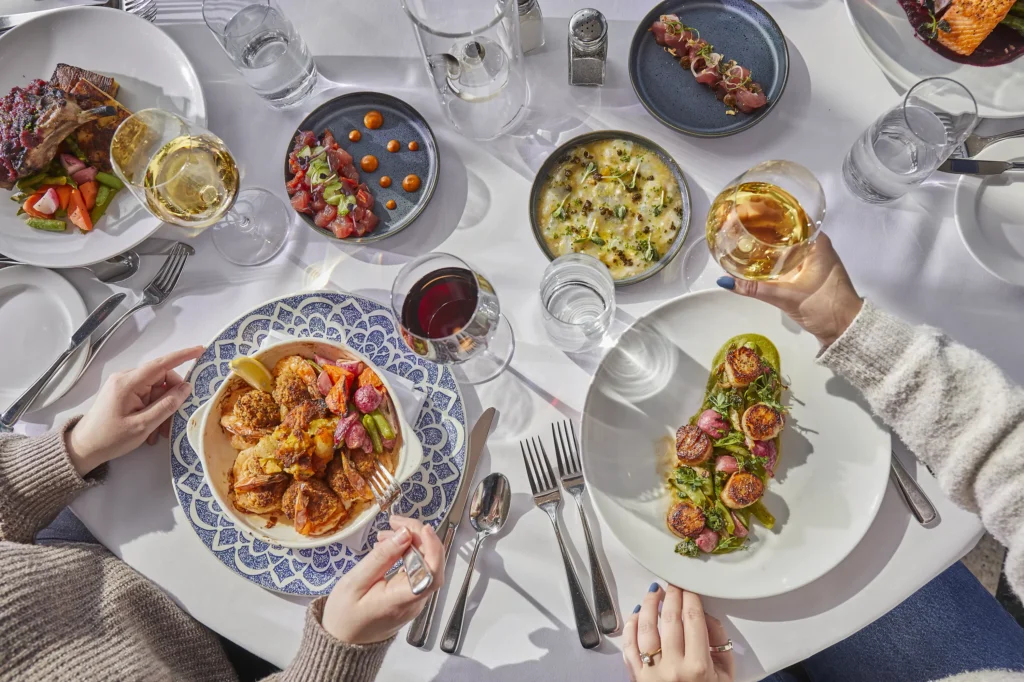An overhead view of diners at a table sharing wine and various seafood dishes including fish and appetizers.
