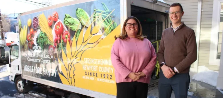 Two people stand in front of a mobile food pantry truck