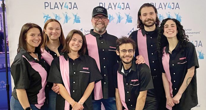 Seven people wearing matching black and pink collared shirts standing together and smiling