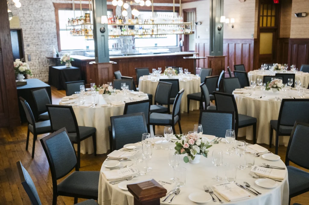Round dining tables set for an event with floral centerpieces and dark chairs inside a dining room.