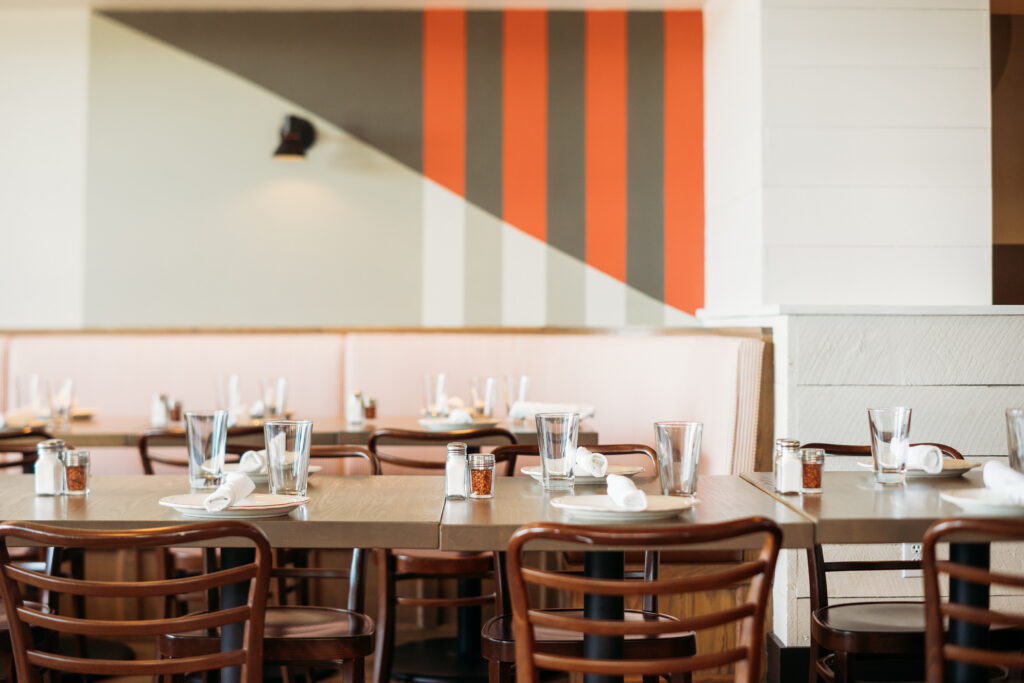 Wooden dining tables set with glasses and place settings in a modern restaurant with orange striped walls.