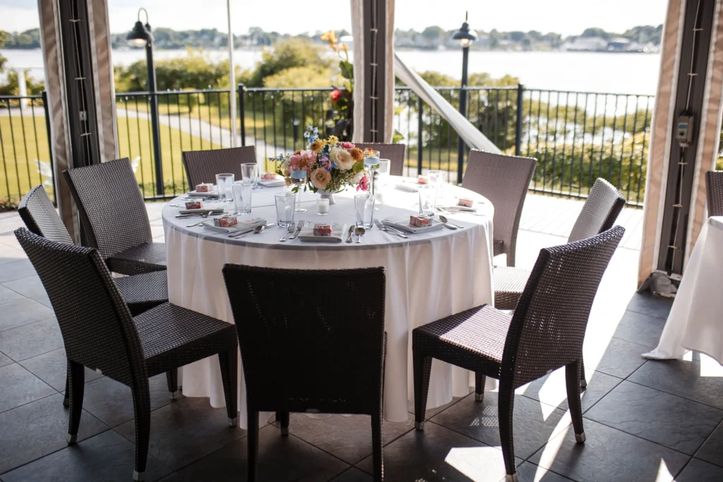 Round table set for a event with chairs on a covered patio overlooking water.