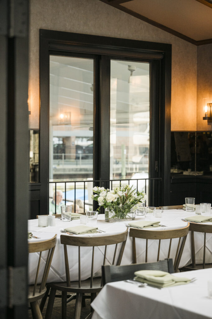 Dining table with white tablecloth, place settings with green napkins, and a white floral centerpiece seen through a dark doorway.