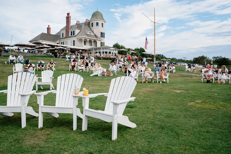 Guests in white Adirondack chairs on the lawn of Castle Hill Inn on a sunny
