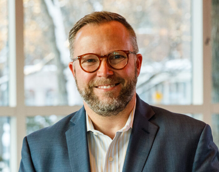 Smiling bearded man wearing glasses and a suit jacket.