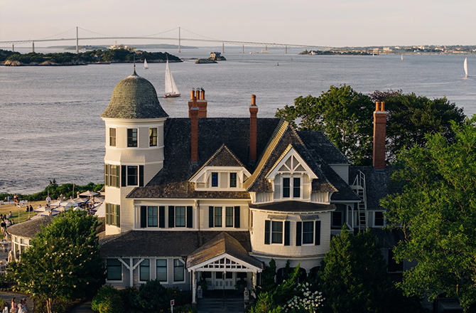 Historic coastal mansion overlooking the water with sailboats in the bay.