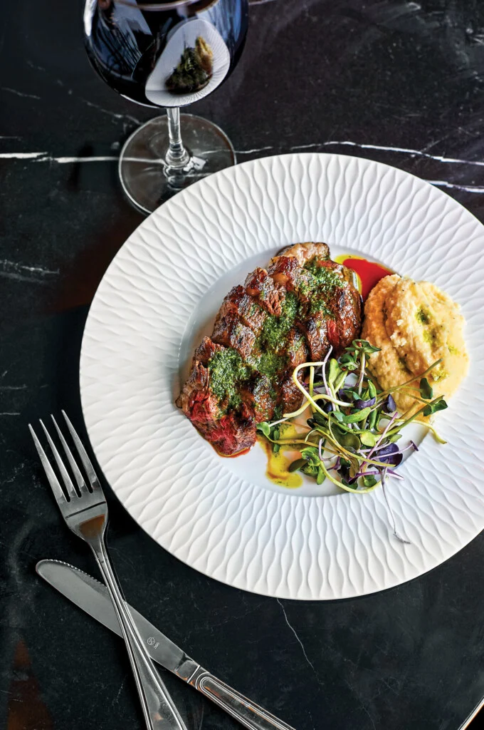 American wagyu picanha sliced and topped with a green sauce with a side of potatoes and red wine