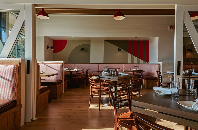 Warmly lit restaurant dining area featuring booths, wooden tables, and red geometric wall decor.
