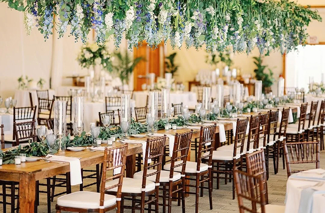 An elaborately decorated long wooden dining table with hanging floral and greenery arrangements overhead.